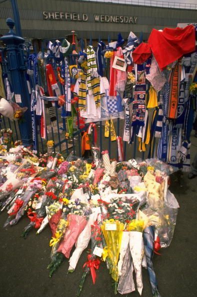 Floral tributes and scarves adorn a fence