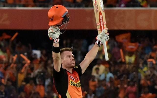 Warner raises his bat to celebrate a century as his fans throng in the background