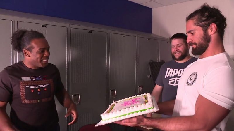 Seth Rollins presenting a cake to Xavier Woods