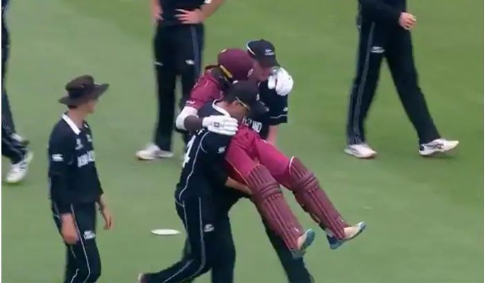 Two New Zealand Under-19 cricketers carry Kirk McKenzie off the field.