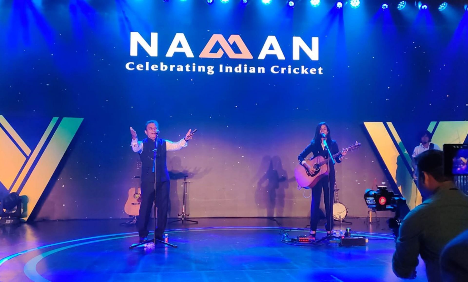 Sunil Gavaskar and Jemimah Rodrigues on the stage singing a song. 