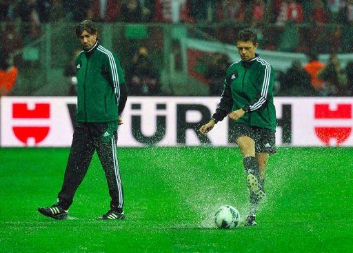 Italian referee Gianluca Rocchi (R) tests the ball on the watercovered pitch at the stadium amid a strong rain