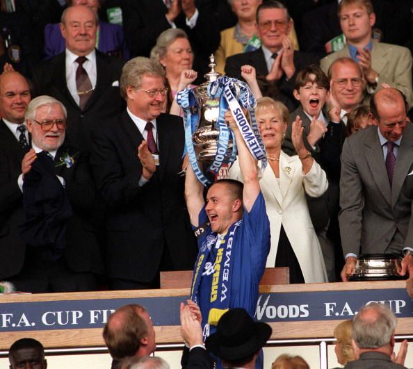 Football. 1997 FA Cup Final. Wembley. 17th May, 1997. Chelsea 2 v Middlesbrough 0. Chelsea captain Dennis Wise proudly holds aloft the trophy after the presentation by the Duchess of Kent, watched by chairman Ken Bates (left) and FA Secretary Graham Kelly