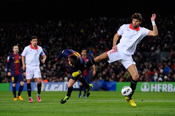 Gerard Pique of FC Barcelona heads the ball towards goal under a challenge by Federico Fazio of Sevilla FC