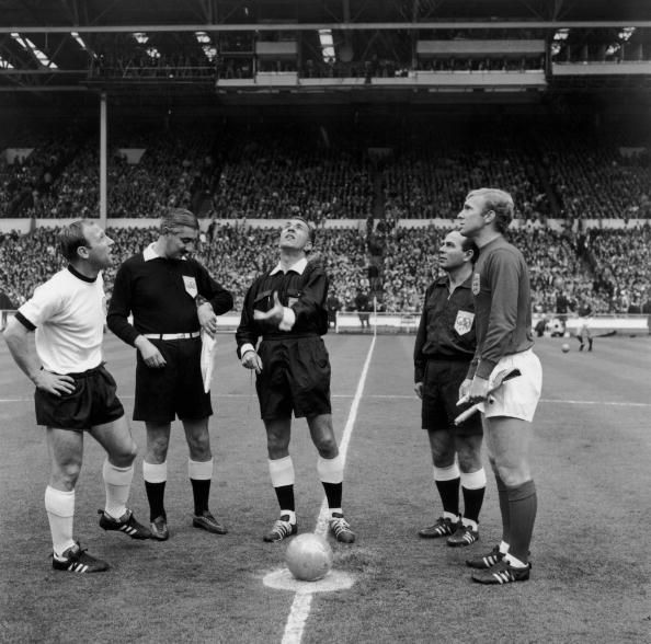 Referee Gottfried Dienst, of Switzerland, tosses the coin before the start of the World Cup final at Wembley between England and West Germany.  He is watched by German captain Uwe Seeler, (left), the Russian linesman Tofik Bakhramov (looking at watch) and English captain Bobby Moore (1941 - 1993) (right).